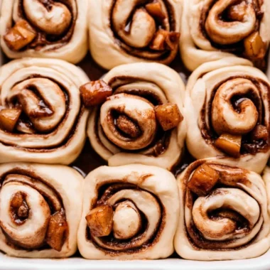 Delicious homemade Apple Pie Cinnamon Rolls drizzled with icing on a wooden table