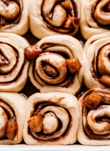 Delicious homemade Apple Pie Cinnamon Rolls drizzled with icing on a wooden table