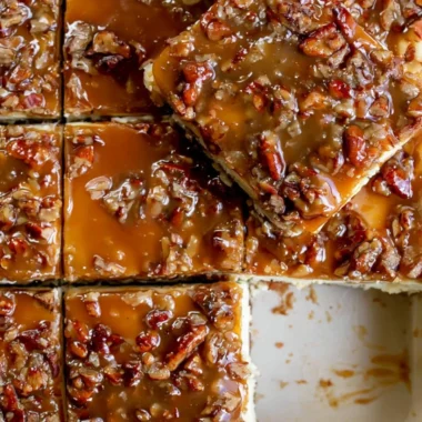 Pecan pie cheesecake bars topped with caramel and pecans on a wooden table